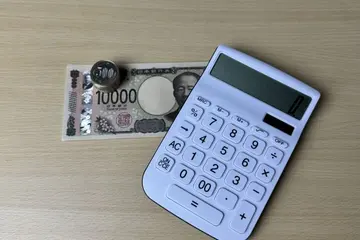白い電卓と一万円札、その上に積んだ500円玉