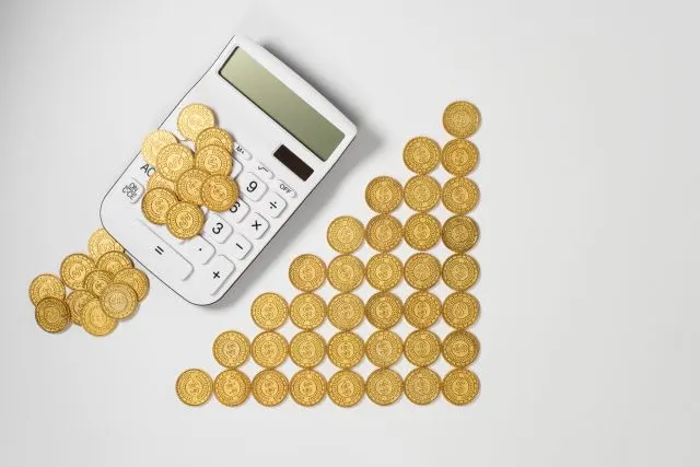 電卓と、右肩上がりの階段状に並べた金色の硬貨