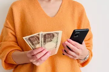 一万円札とスマートフォンを手に持つ女性